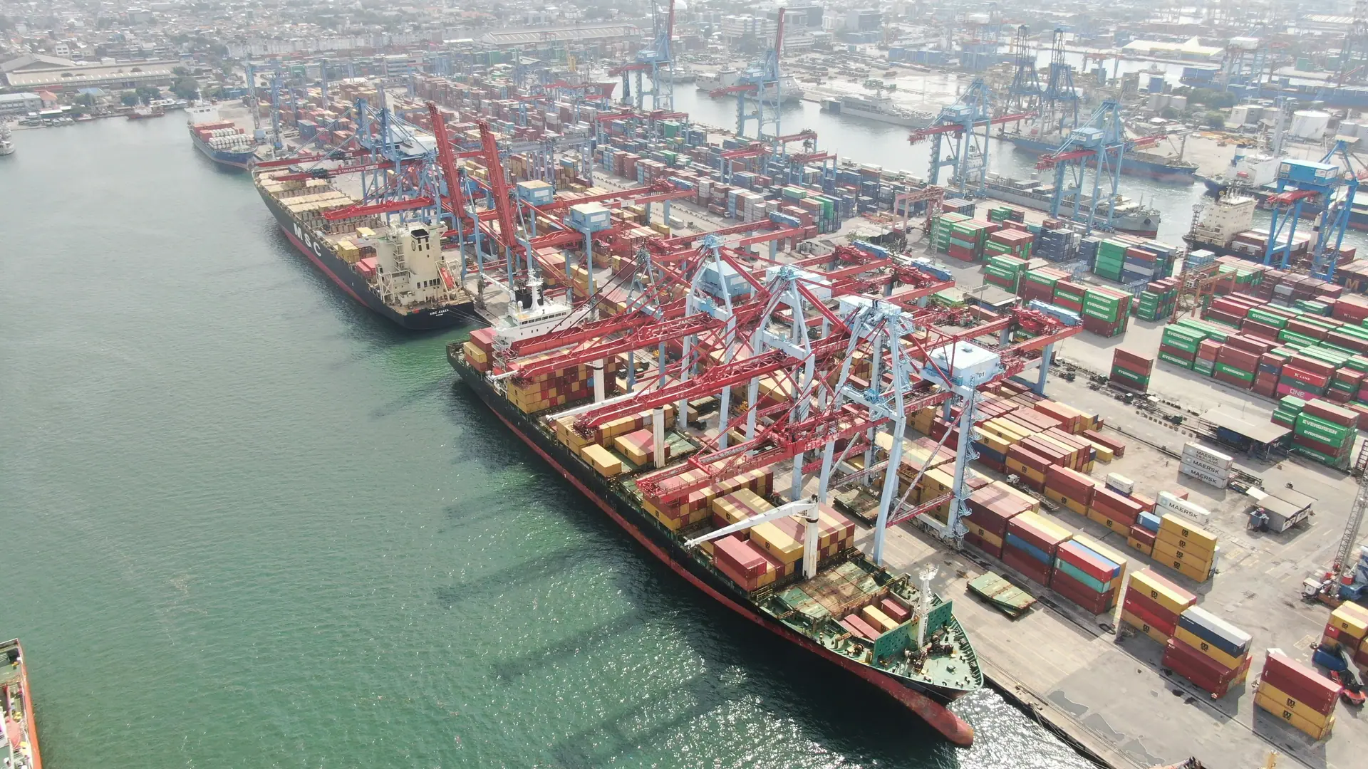 Aerial view of a container terminal with vessels alongside and stacked containers.