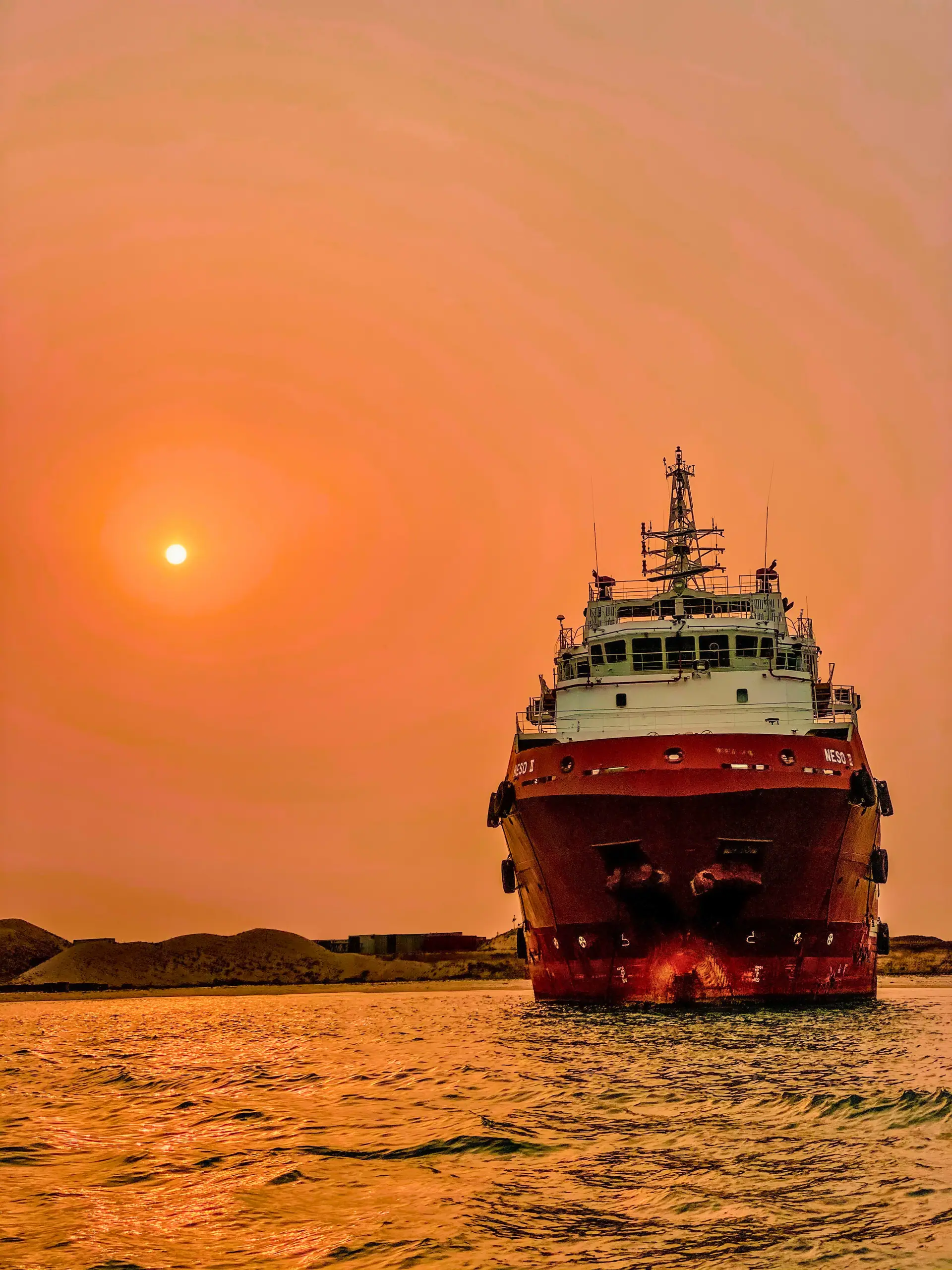 Marine support vessel under way at sunset on open water.